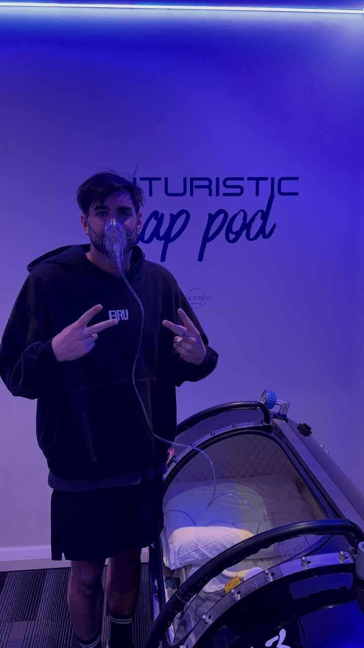 Person wearing an oxygen mask beside a hyperbaric chamber.