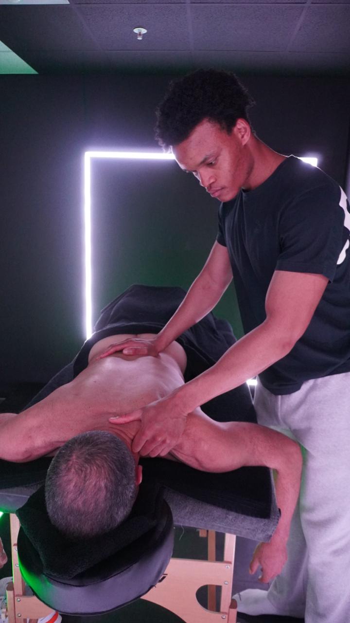 Sports massage therapist working across a client’s upper back and shoulder